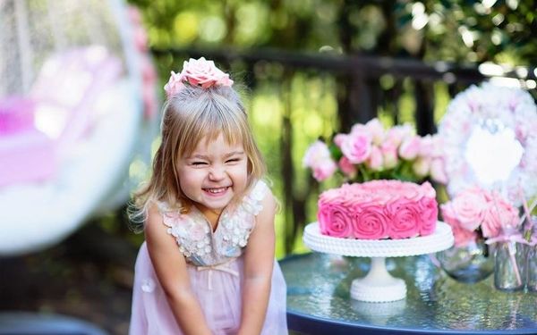 Kleines Mädchen mit rosa Kleid lacht neben einer pinken Geburtstagstorte.