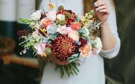 Braut hält einen großen, herbstlich inspirierten Blumenstrauß mit Chrysanthemen.