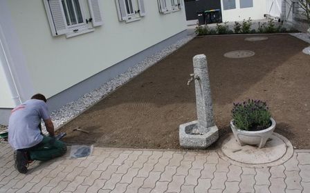 Mann kniet vor einem modernen Gebäude und gestaltet eine Fläche mit Kies.