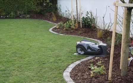 Frisch angelegter Garten mit geschwungenen Beeten, Rasenmähroboter in Betrieb.