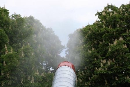 Große Nebelmaschine stößt dichten weißen Dampf in eine grüne Baumlandschaft.