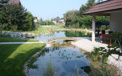 Natürlicher Schwimmteich mit Brücke und angrenzendem Garten.