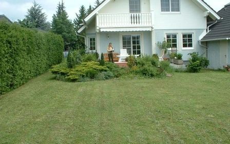 Gepflegter Garten mit Rasenfläche vor einem weißen Einfamilienhaus.
