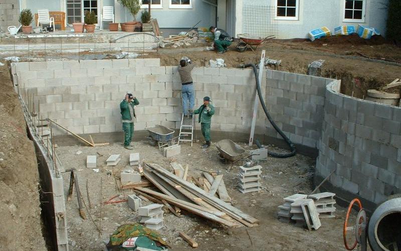 Baustelle eines Schwimmteichs mit drei Arbeitern beim Mauern.