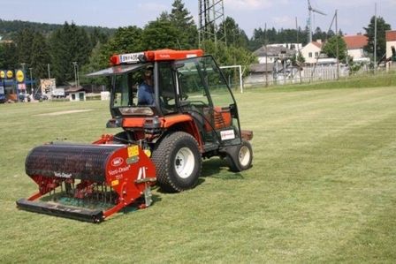 Roter Traktor bei der Rasenpflege auf einer Sportanlage.