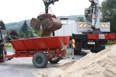 Bagger lädt Sand in einen Streuwagen, der für die Rasenpflege genutzt wird.