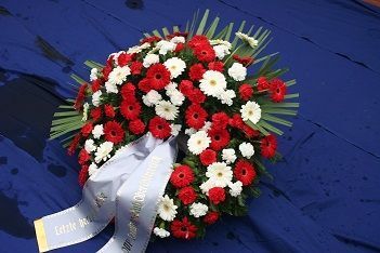 Blumengesteck mit roten und weißen Blumen, dekoriert mit einer weißen Schleife.