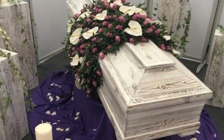 Weißer Sarg mit Blumen und Kerzen für eine Beerdigung.