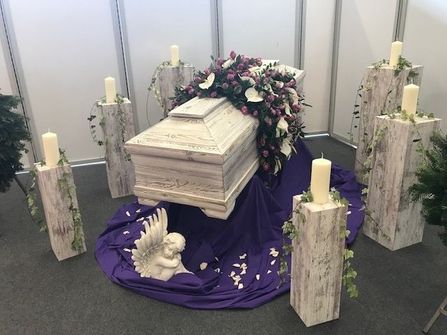 Weißer Sarg mit Blumendekoration in einer Trauerhalle.