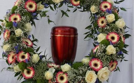 Kranz mit bunten Blumen und Urne in der Mitte.