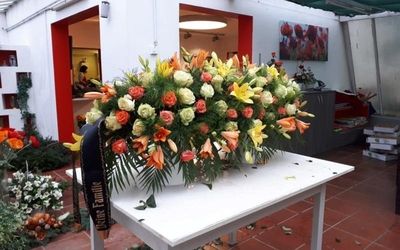 Großer Trauerkranz mit roten und orangefarbenen Rosen auf einem Tisch.