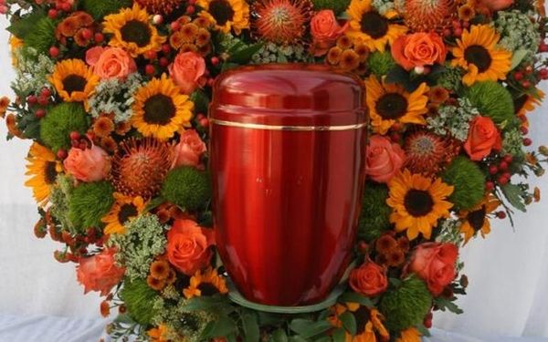 Urne inmitten eines herbstlich gestalteten Kranzes mit Sonnenblumen und Rosen.